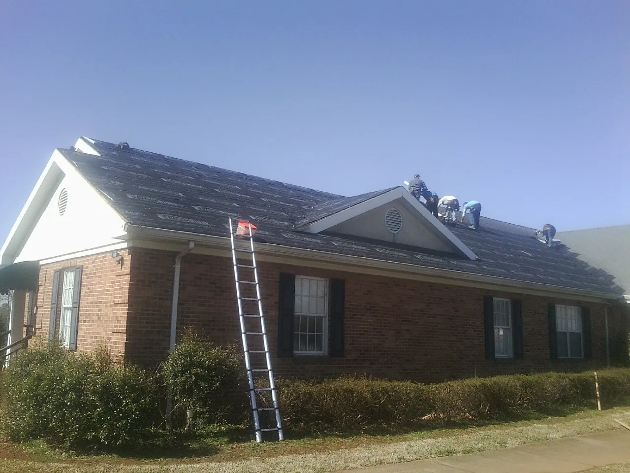 Crew tearing shingles off a brick ranch roof with a ladder set — Emergency Roof Repair work by our crew in Weare