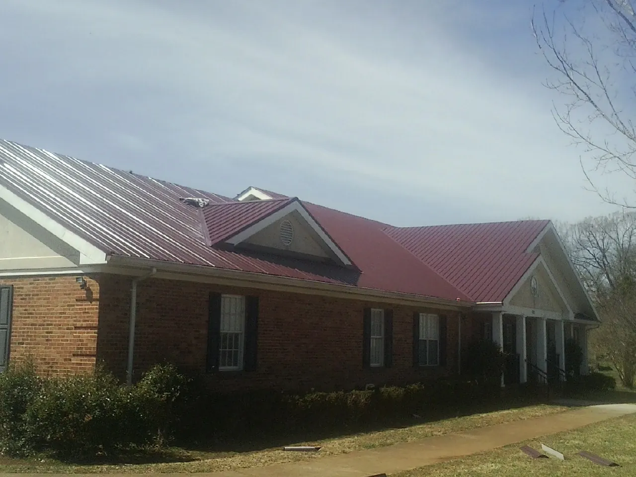 Red metal roof with gabled entries on a long brick building, from a Hail Damage Roof Repair job in Weare