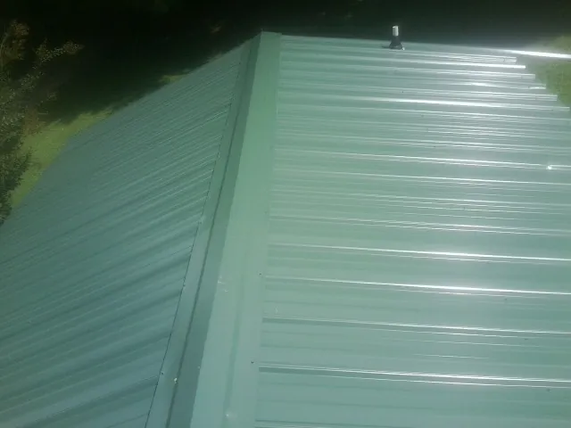 New green metal panels meeting at the ridge of a roof — Flat Roof Repair work by our crew in Weare