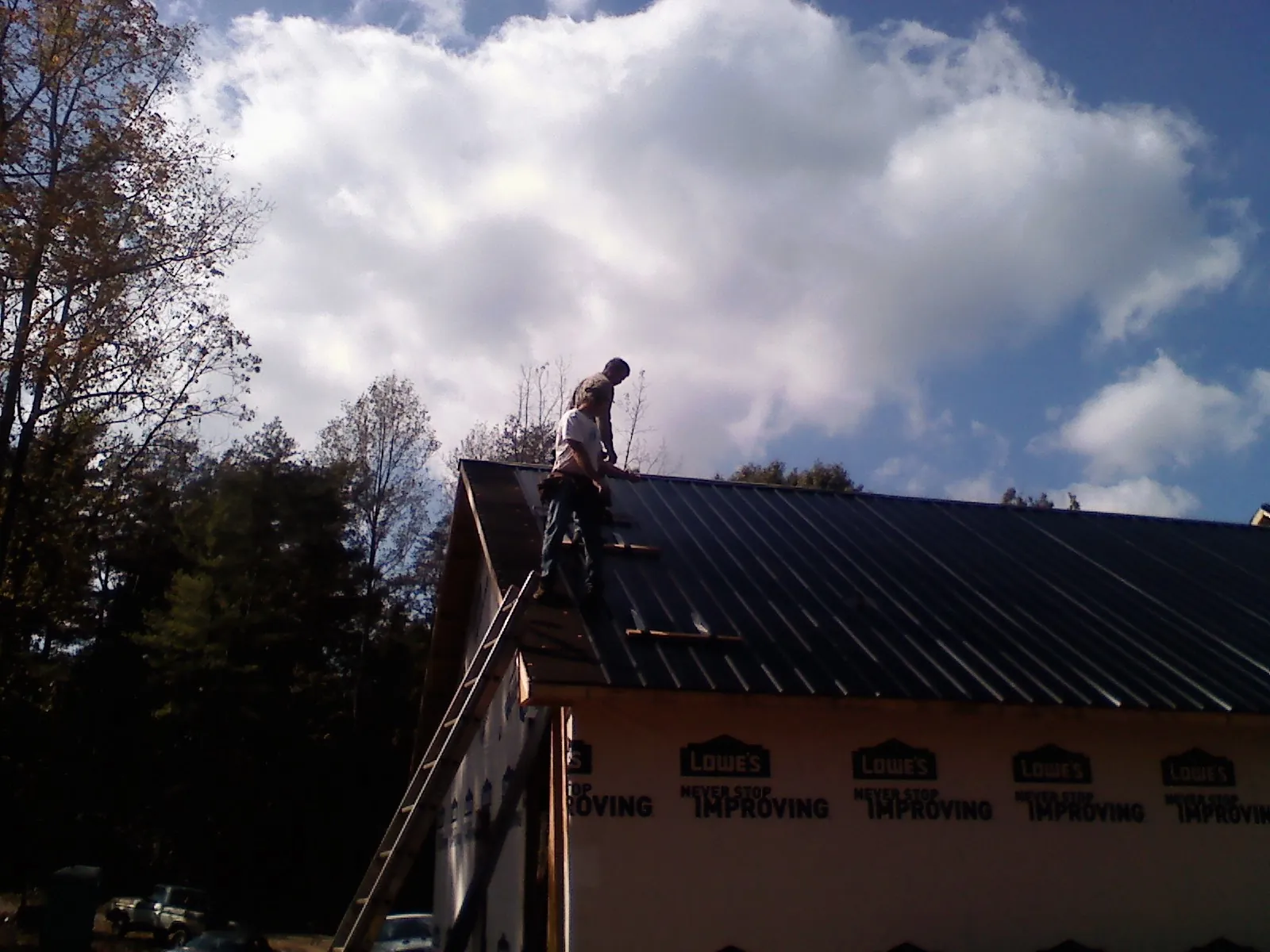 Roofer fastening dark metal panels high against a cloudy sky, from a Roof Inspection job in Weare