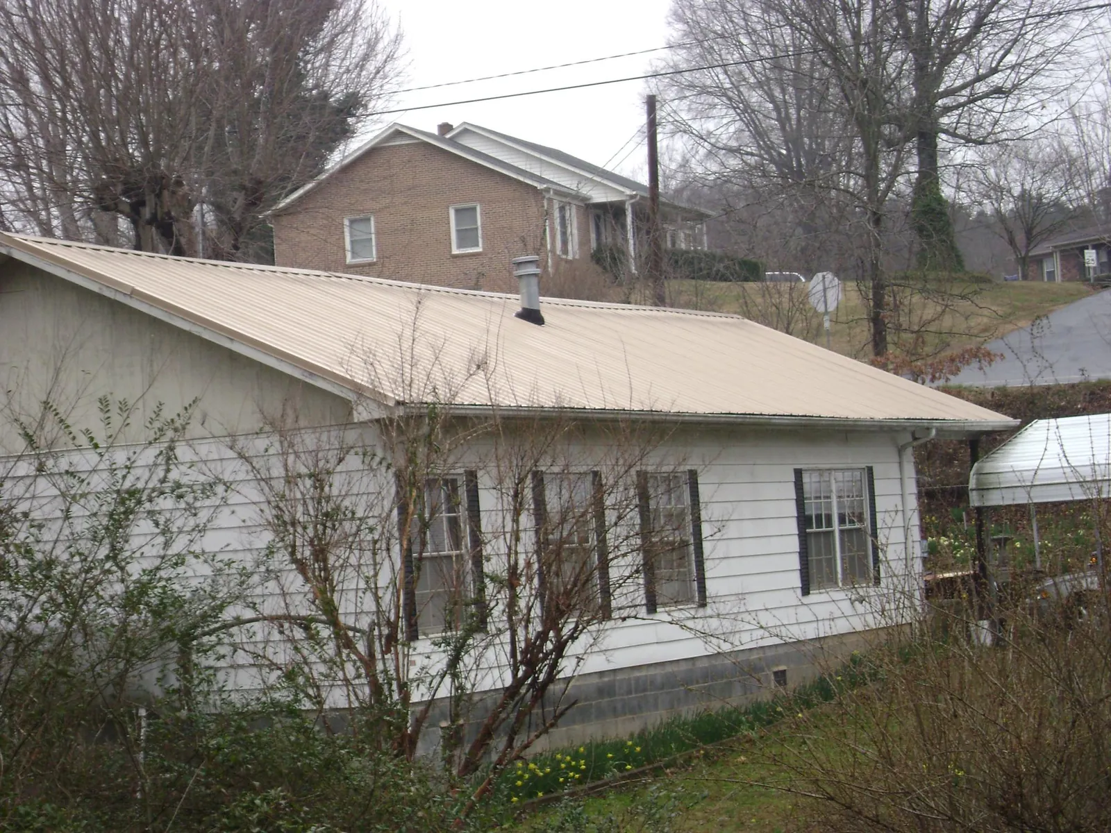 Tan metal roof on a white sided house set into a hillside — Commercial Roofing by Roofing Brothers in Weare