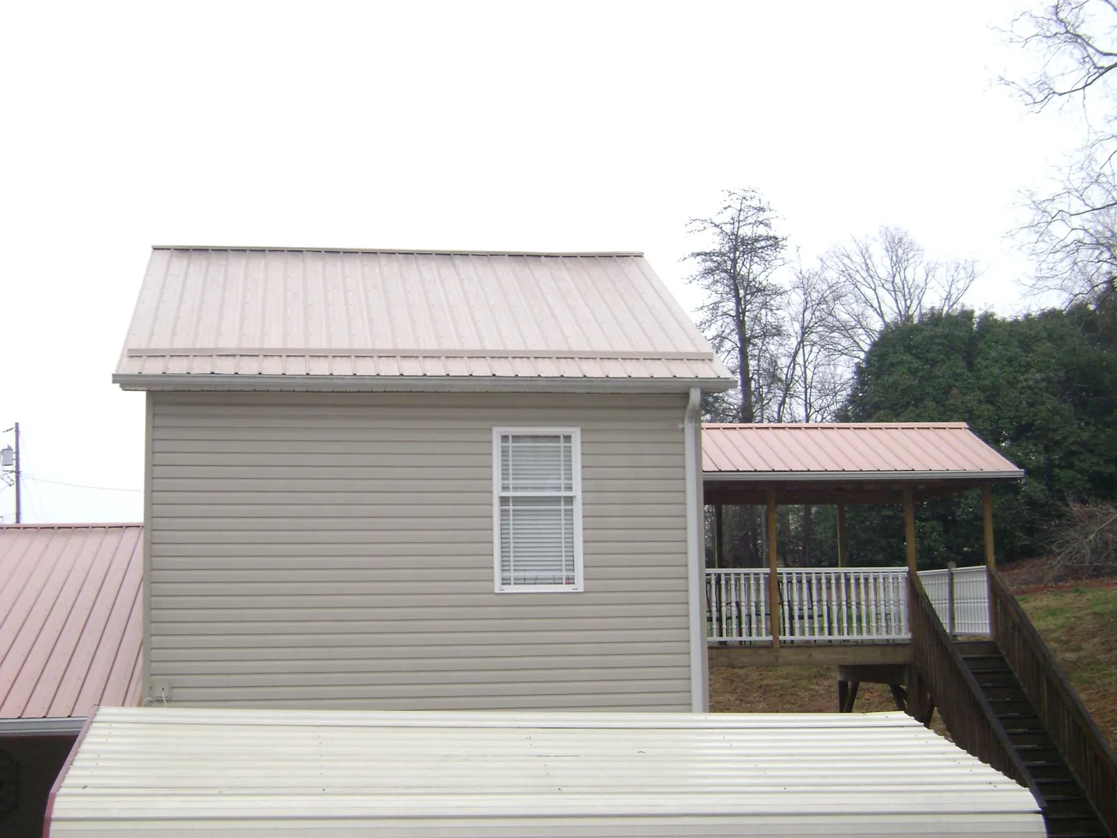Tan metal roofs on a two story addition and attached porch, from a Roof Replacement job in Weare