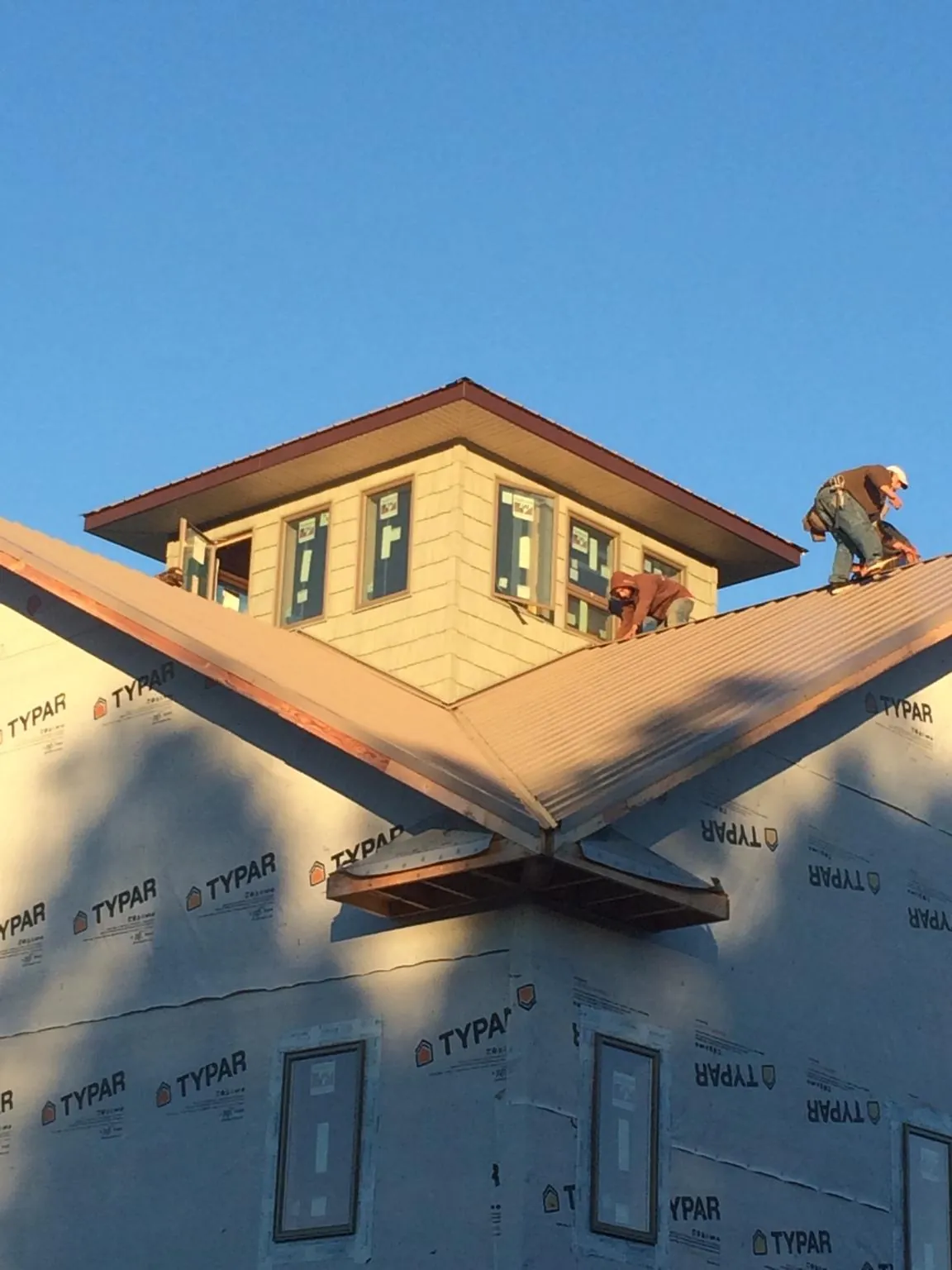 Roofers working around a rooftop cupola on a new metal roof at sunset in Weare